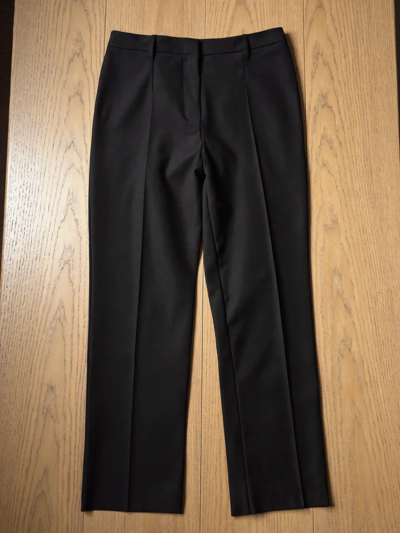 Schwarze Hose mit Bügelfalte flach auf einem hellen Eichentisch
